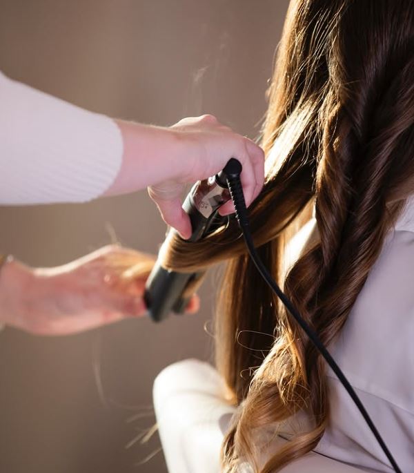 en frisör lockar en kunds hår med en plattång
